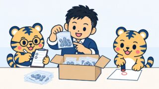 紺の線画イラスト。経営者が開けた段ボール箱から部品の袋を取り出して数え、横で丸眼鏡の虎がクリップボードに丸印を付け、もう1体の虎が無地の紙に朱色の判子を押している